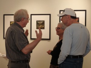 Dan Burkholder describes his working methods to some gallery visitors. One of his images is on the wall.